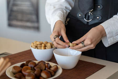 woman's hands peeling peanuts over a bowl in the kitchen, close-up horizontal viewの写真素材
