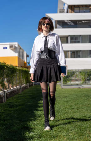 young girl in uniform walking on the lawn in front of a building, front view, vertical imageの写真素材