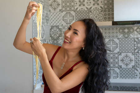 smiling woman holding pasta up and looking at it, horizontal background with patterned tilesの写真素材