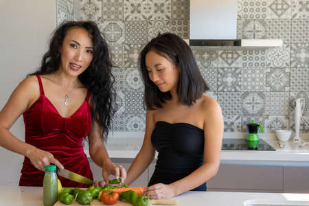 two women cooking in the kitchen wearing dresses, one of them cutting vegetables, horizontal patterned backgroundの写真素材