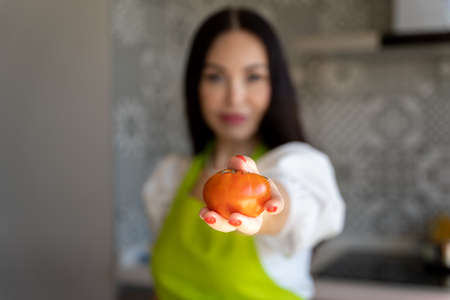 Soft focus of woman demonstrating fresh tomato to camera while preparing healthy food for lunch at homeの写真素材