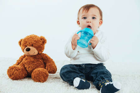 Stock studio photo with a white background of a baby with a canteen with handles and a teddy bear.の写真素材