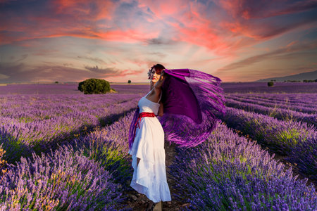 Woman looking at the camera while posing outdoors in a colorful lavender flower field at sunset. Nature concept.の写真素材