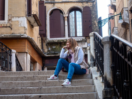Relaxed tourist woman sitting on the stairs on a bridge in the city of Venice, Italy. Tourism concept.の写真素材