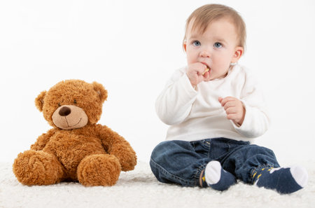 Stock studio photo with the white background of a baby with fingers in the mouth with a teddy bearの写真素材