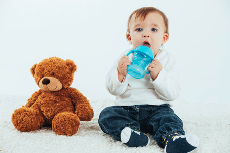 Stock studio photo with a white background of a baby with a canteen with handles and a teddy bear.の写真素材