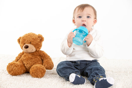 Stock studio photo with a white background of a baby with a canteen with handles and a teddy bear.の写真素材