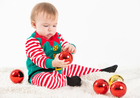 Stock studio photo with white background of a baby in elf costume grabbing christmas ballsの写真素材