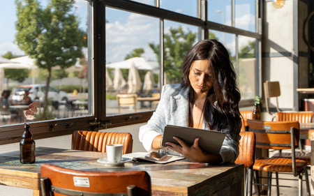 Woman using a digital tablet while sitting in a coffee shop. Technology and business concept.の写真素材