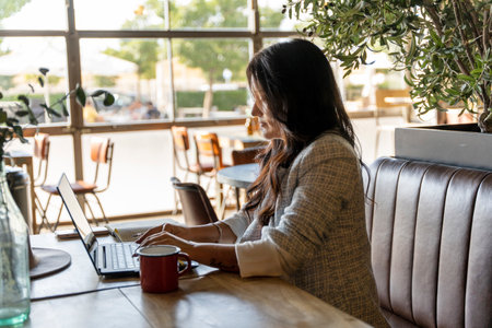 Woman typing on a laptop computer while working in a coffee shop. Technology, business and freelance concept.の写真素材