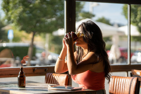 Woman with sunglasses drinking a cup of coffee while relaxing sitting in a coffee shop.の写真素材