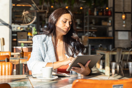 Shocked woman looking with surprise at the digital tablet while sitting in a coffee shop. Technology concept.の写真素材