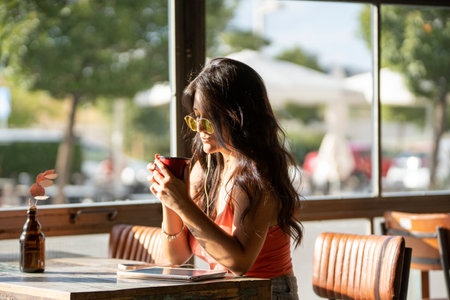 Woman with sunglasses drinking a cup of coffee while relaxing sitting in a coffee shop.の写真素材