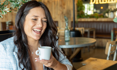 Close up view of a joyful woman smiling while enjoying drinking a cup of coffee in a coffee shop.の写真素材