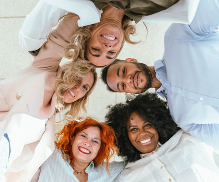 Low angle view of diverse business colleagues embracing and smiling while standing in circle. Business and teamwork concept.の写真素材