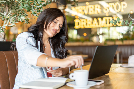 Woman stirring a coffee while working sitting in the coffee shop. Technology and business concept.の写真素材