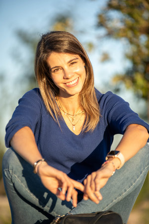 Relaxed woman looking at camera and smiling while enjoying outdoors in a park during sunset.の写真素材