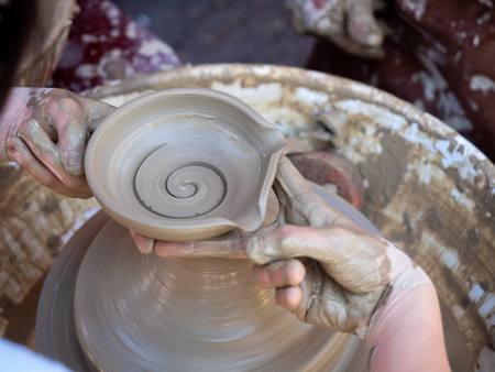 Potter helps a girl with his hands to create a clay pot on the latheの写真素材