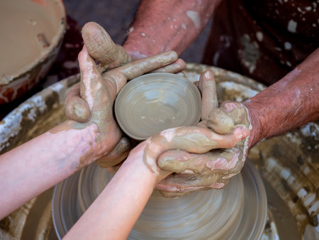 Potter helps a girl with his hands to create a clay pot on the latheの写真素材