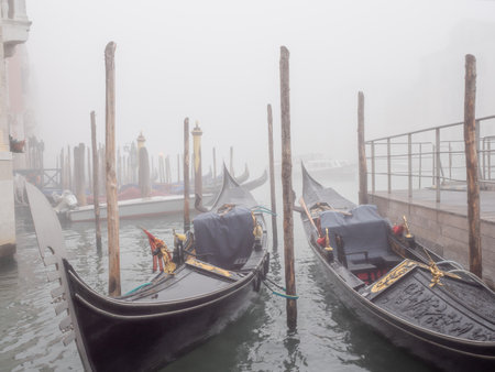 Gondolas moored on the pier in Venice on a foggy day. Transportation concept.の写真素材