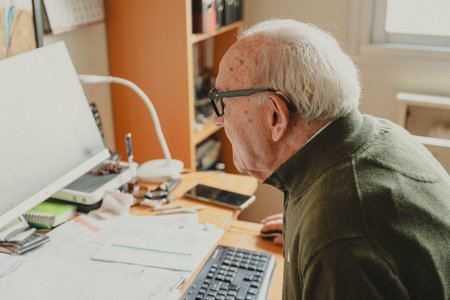 Elderly man actively engaging with a computer, using the internet on a desk