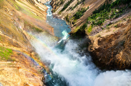 Mist from the powerful Lower Falls in Yellowstone National Park creates a vivid rainbow over the Grand Canyon of the Yellowstone, adding color to the rugged landscape. UNESCO world heritage in Wyomingの写真素材
