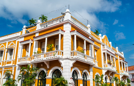 Vibrant colonial building with white columns and balconies stands in the historic district of Cartagena, Colombia, its bold orange facade glowing under a bright blue sky and tropical sunlightの写真素材
