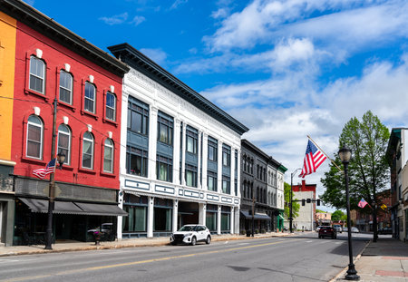 A row of red, white, and gray 19th-century storefronts lines Water Street in Augusta, Maine, United States, where American flags flutter beneath a bright spring sky.の写真素材