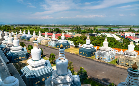 Rows of white stupas line a quiet pathway at Fo Guang Shan Monastery in Kaohsiung, Taiwan, with a traditional Chinese pagoda visible through the trees under a clear blue skyの写真素材