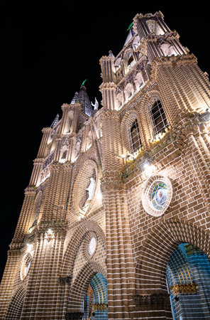 Low-angle night view of Jardins brick Basilica of the Immaculate Conception, its ornate neo-gothic facade, arches, and soaring spires brilliantly floodlit against a pitch-black skyの写真素材