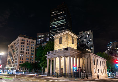 Kings Chapel in Boston, Massachusetts, United States, stands brightly lit at a quiet downtown intersection, its stone portico and columns contrasting with modern high rises under a clear spring night skyの写真素材