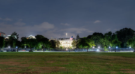 The White House, the official residence of the U.S. President, viewed from The Ellipse in Washington, D.C., United States. The historic neoclassical building is illuminated at night behind a security fenceの写真素材