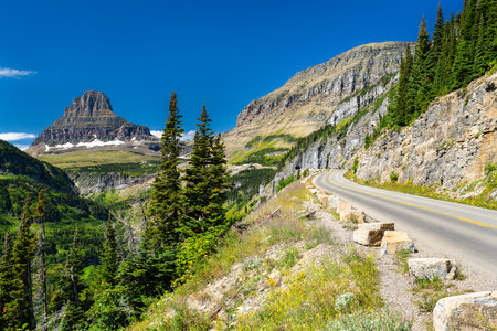 Scenic view of the winding Going-to-the-Sun Road in Glacier National Park, Montana. The iconic Clements Mountain rises in the distance under a clear blue sky. Represents travel and natureの写真素材