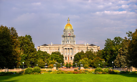 Colorado State Capitol building in Denver, Colorado. The gold dome is lit by evening sun, with a green lawn and park in the foreground under a cloudy skyの写真素材