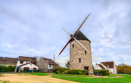 The historic Moulin de Montfermeil or Sempin Windmill in France. The stone structure with wooden blades stands in a park, surrounded by houses under a cloudy skyの写真素材