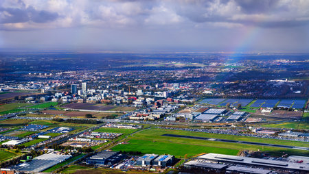 Aerial view of the landscape around Hoofddorp and Schiphol Airport in the Netherlands. A rainbow arches over the green fields, runways, and buildings under a dramatic cloudy skyの写真素材