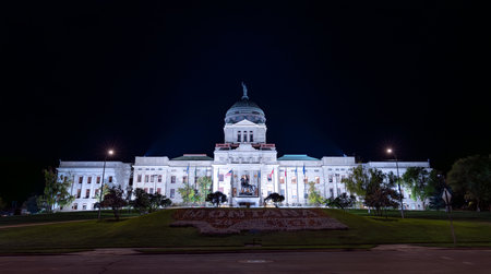 The Montana State Capitol in Helena is illuminated at night. The bright lights highlight the stone facade and dome, contrasting with the dark skyの写真素材