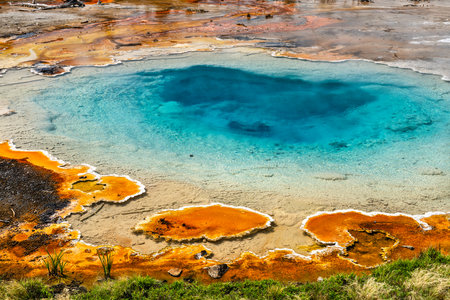 Colorful Silex Spring bubbles with hot blue water in Yellowstone National Park Wyoming. Geothermal feature displays vibrant orange bacterial mats contrasting with deep turquoise pool on sunny dayの写真素材