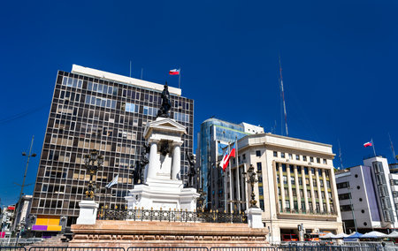 Historic Monument to the Heroes of Iquique stands in Plaza Sotomayor of Valparaiso, Chile. Bronze statues and white pedestal honor naval heroes under clear blue sky near Chilean Navy headquartersの写真素材