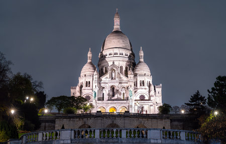 Illuminated Sacre-Coeur Basilica stands on Montmartre hill in Paris, France. Historic white stone church features large dome and Roman-Byzantine architecture in Ile-de-France regionの写真素材