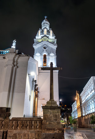 Quito Metropolitan Cathedral stands on Plaza Grande in historic center of Quito Ecuador. White colonial church features stone cross and illuminated bell tower under night skyの写真素材