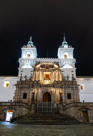 Church of San Francisco stands on cobblestone plaza in Quito, Ecuador. Historic colonial complex features twin towers and stone facade in UNESCO World Heritage center under night skyの写真素材