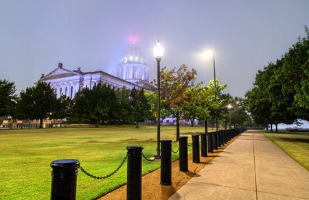 Oklahoma State Capitol building in Oklahoma City. Neoclassical government architecture features an illuminated dome obscured by heavy fog and a walkway with black bollards at nightの写真素材