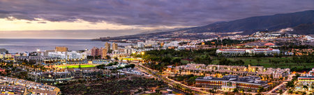 Scenic panoramic twilight view of the illuminated city streets, stadium, and seaside resorts of...