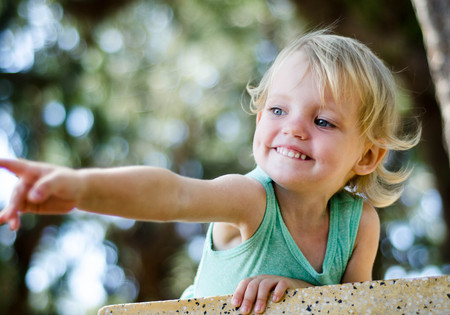 Adorable toddler girl smiling and  pointing somewhere above the camera.の写真素材
