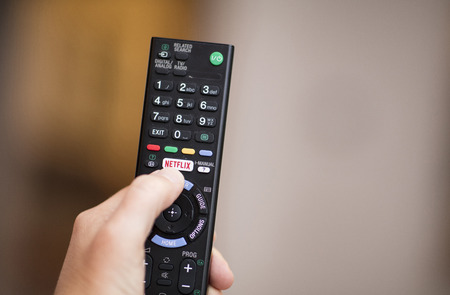 A person using a television remote with a dedicated Netflix logo on the button - February 2018