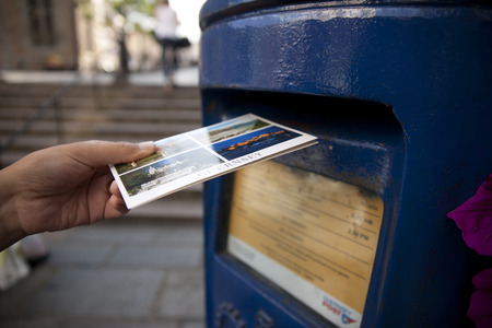 a Hand putting a postcard in a Blue Guernsey Post Box unique to Guernsey in the town of St Pierre...