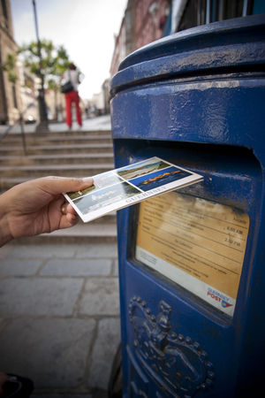 a Hand putting a postcard in a Blue Guernsey Post Box unique to Guernsey in the town of St Pierre...
