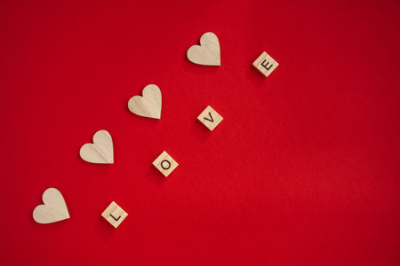 The word love consists of wooden letters, above each letter there is a wooden heart on a bright red background. The concept of love and valentines day, happy family, wedding, fidelity, February 14.の写真素材