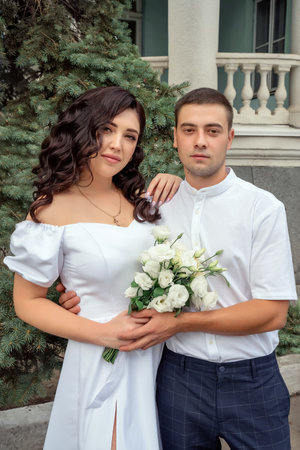 Gorgeous woman with dark hair in luxurious wedding dress and her handsome husband posing near the wedding palace. love story, wedding photo of beautiful coupleの写真素材